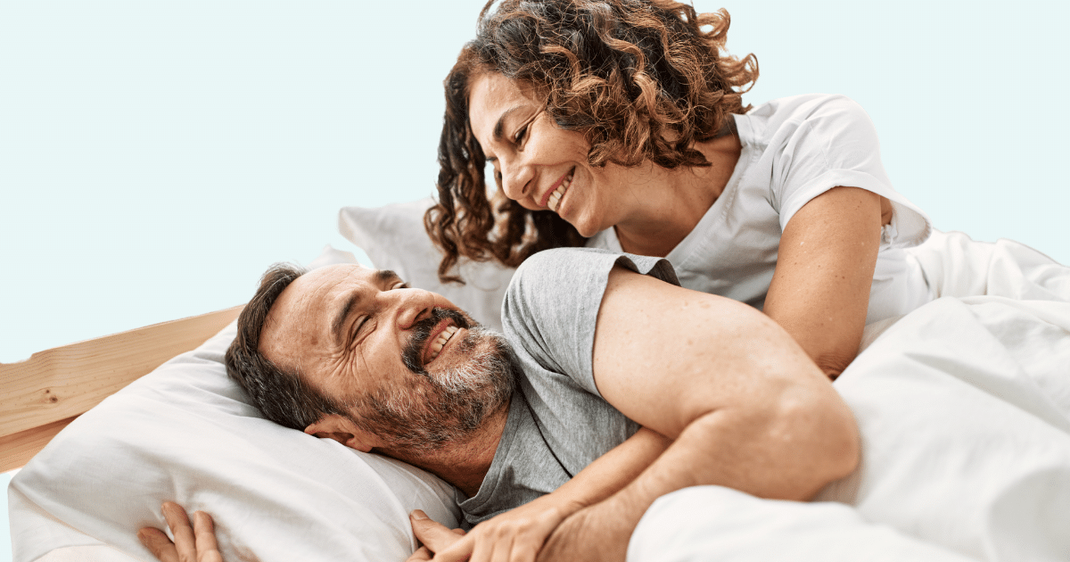 middle-aged couple cuddling in a bed while looking at each other and smiling