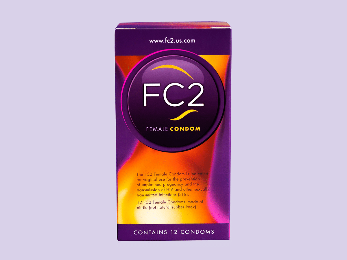 A box of FC2 female condoms is displayed against a light purple background. The box is predominantly purple and orange, with text indicating that it contains 12 condoms